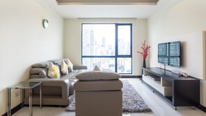 Una sala de estar moderna con un sofá, una mesa de centro de vidrio, un mueble de entretenimiento negro y un ventanal con vista a la ciudad.