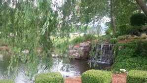 Ein friedlicher Garten mit Teich, einem kleinen Wasserfall und ordentlich geschnittenen Hecken.