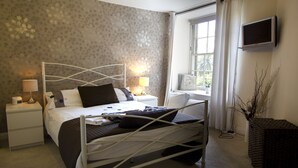 Ein Schlafzimmer mit einem Bett, Nachttischen, einem Fernseher und einem Fenster mit Vorhängen.
