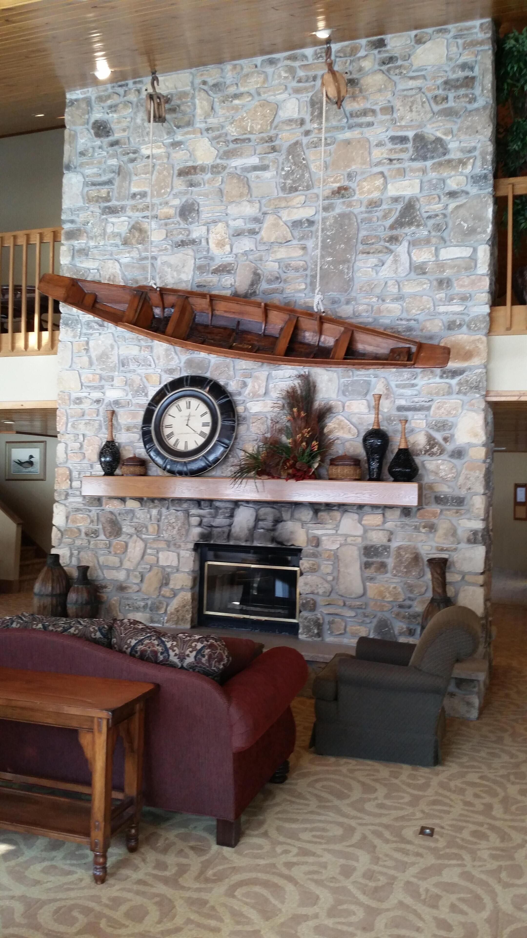 Una chimenea de piedra con un reloj, estanterías con adornos y una zona de estar con mesa de madera y sofás.