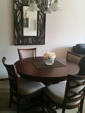 A round dining table with six chairs, a vase with flowers, and a decorative wall piece above.
