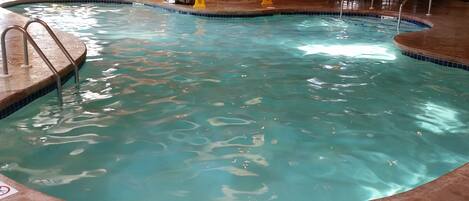 Une piscine intérieure à l'eau claire, avec un bord carrelé et une terrasse en bois qui l'entoure.
