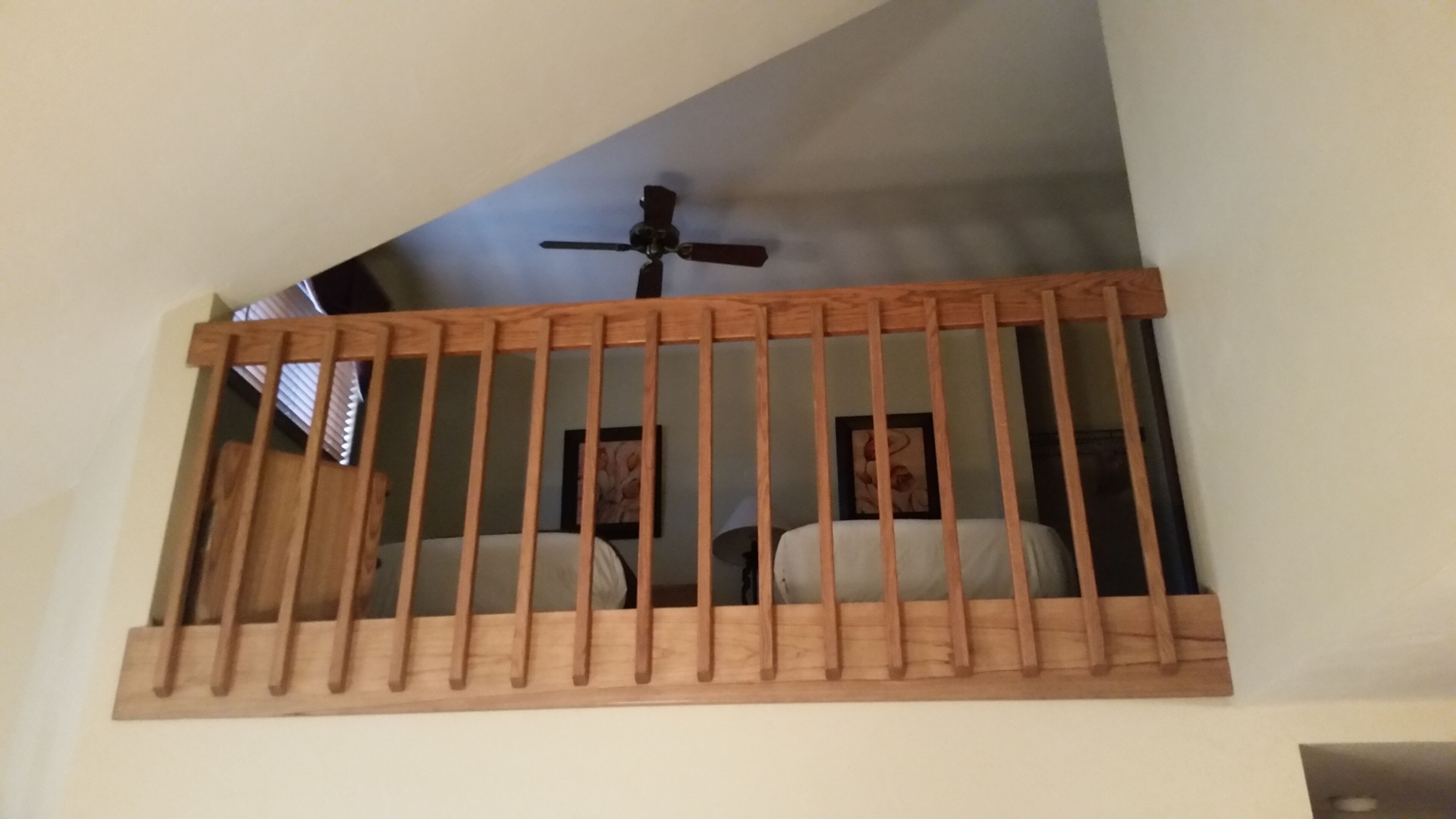 Une balustrade en bois sur un balcon, avec un ventilateur de plafond au-dessus.