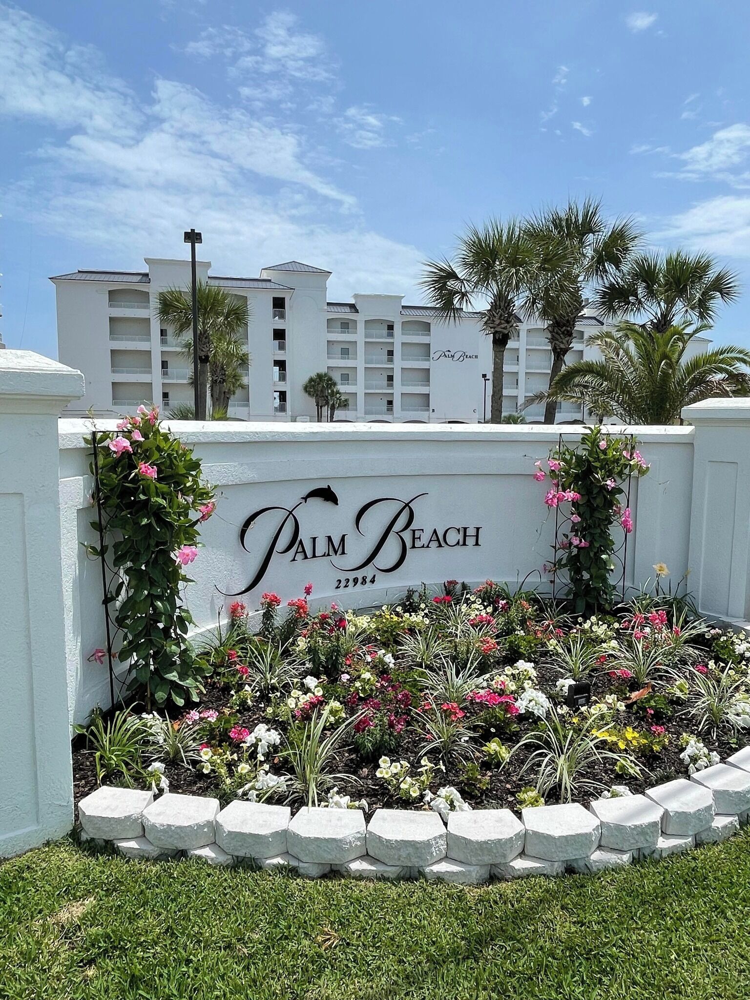 A sign for Palm Beach with a landscaped garden in front.