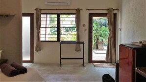 A room with a bed, a small table, an air conditioner, and a view of greenery outside. - Fern House Retreat (Chalong)