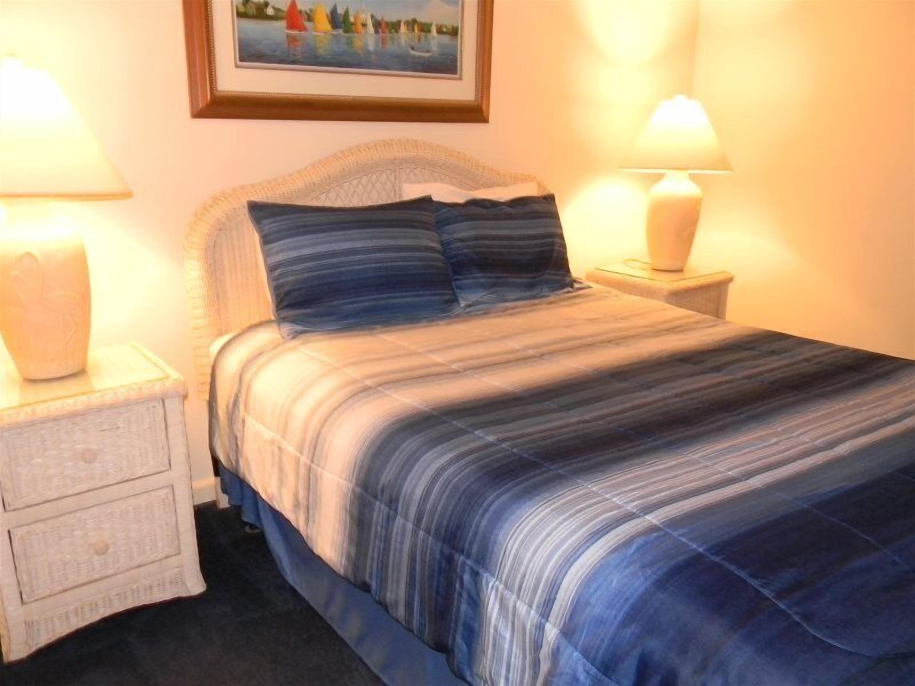 Een netjes opgemaakt bed met gestreept beddengoed, twee nachtkastjes met lampen en een ingelijst beeld aan de muur.