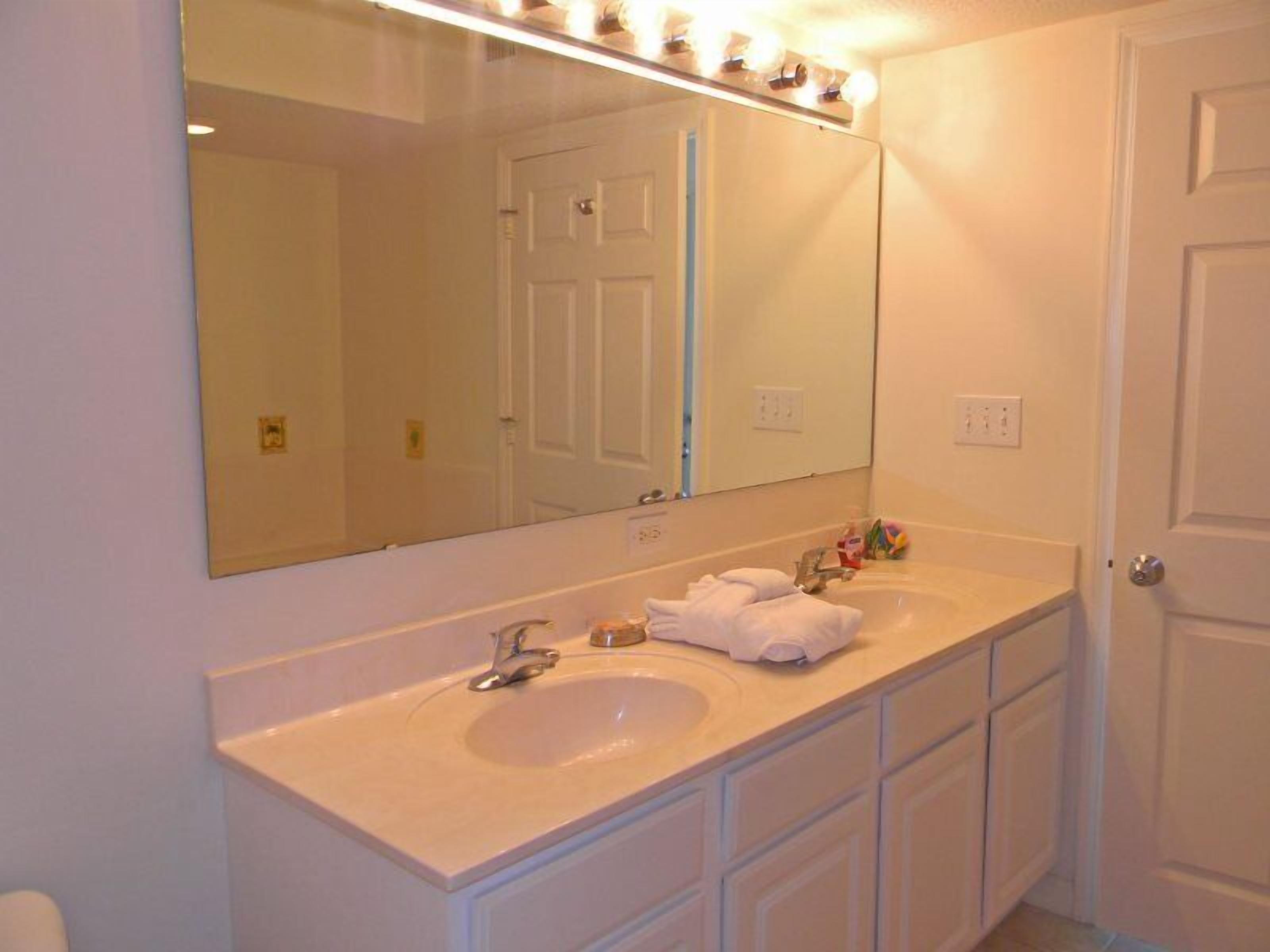 A bathroom with a large mirror, two sinks, and a door.