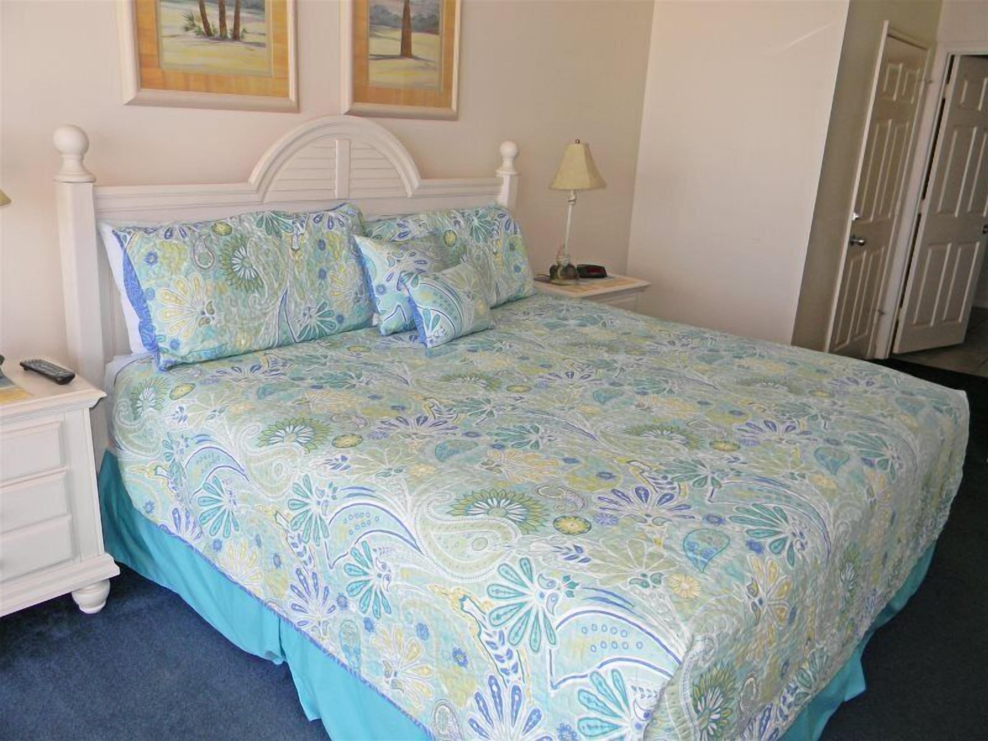 Un dormitorio con cama, mesitas de noche, una lámpara y una puerta.
