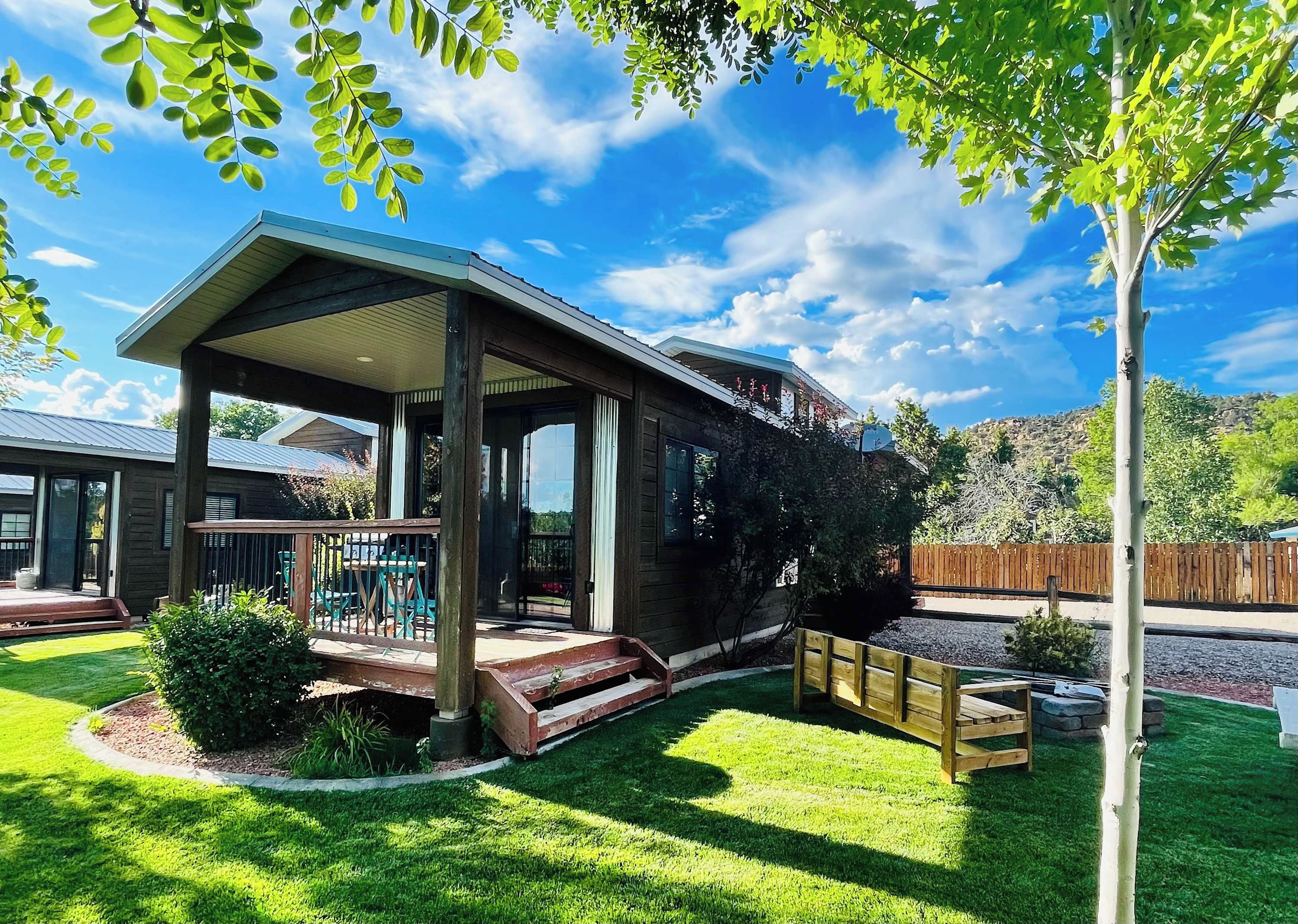 A two-story wooden house with a covered patio, a fenced backyard, and a view of a mountainous landscape.