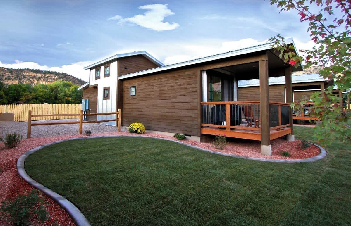 Ein zweistöckiges Holzhaus mit überdachter Veranda und einem angelegten Garten.