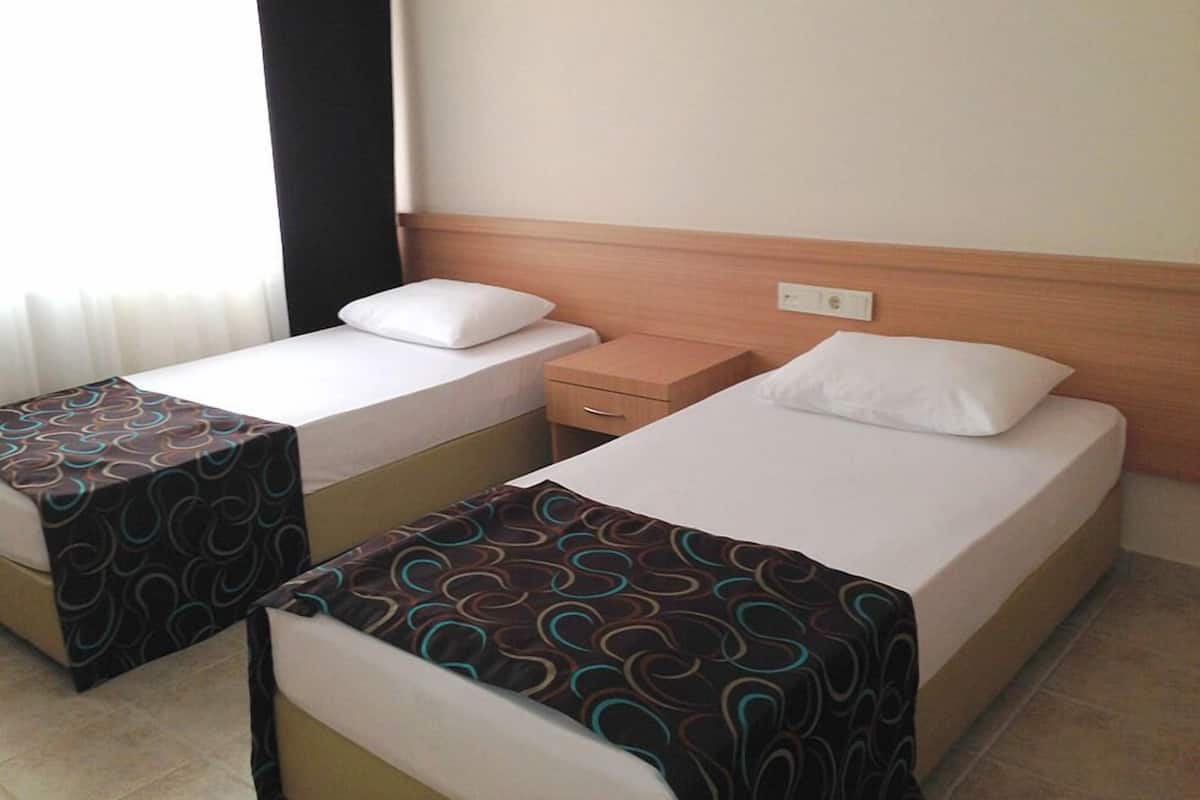 A hotel room with two single beds, each with a patterned bedspread, a wooden headboard, and a nightstand with a drawer.