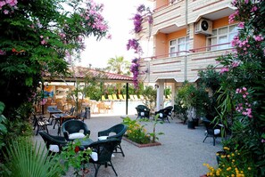 An outdoor patio area with wicker furniture, potted plants, and a pool in the background. - Beyaz Saray Hotel (Manavgat)