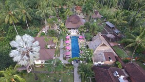 An aerial view of a resort with a central swimming pool, multiple buildings with thatched roofs, and lush tropical vegetation. - Puri Mas Spa Resort (Senggigi)