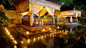 A traditional wooden structure with a thatched roof, surrounded by a water body reflecting lights. - Puri Mas Spa Resort (Senggigi)