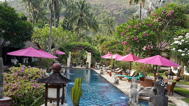 A pool area with lounge chairs and umbrellas, surrounded by tropical plants and statues. - Puri Mas Spa Resort (Senggigi)