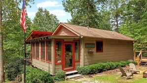 A small cabin with a red door and windows, surrounded by greenery.