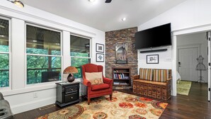 A living room with a fireplace, a TV mounted on the wall, and a large window overlooking greenery.