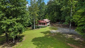 A cabin surrounded by dense forest, with a well-maintained lawn and a wooden deck.