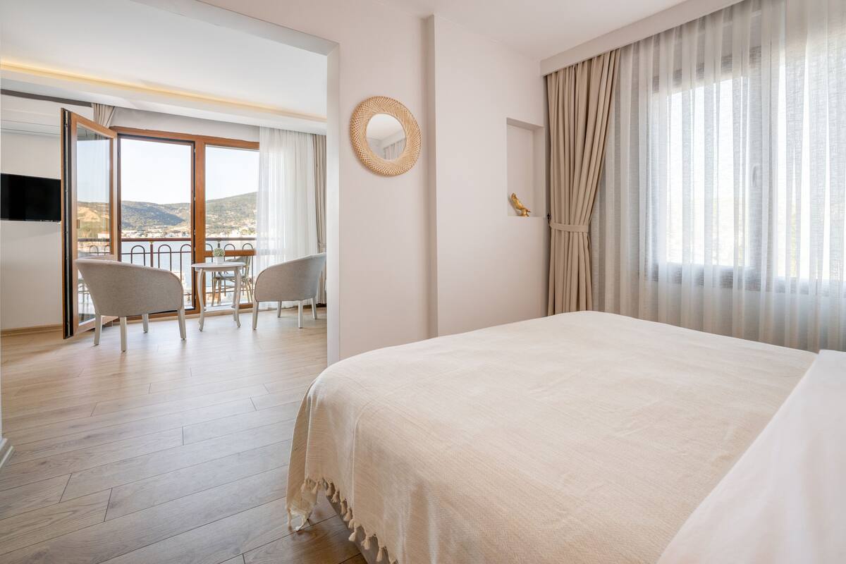 Ein Hotelzimmer mit einem großen Bett, einem Balkon mit Aussicht, einem Essbereich und einem Fernseher.