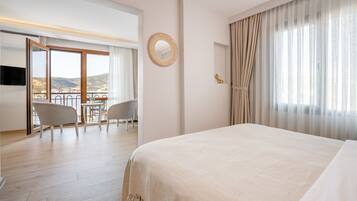 Habitación de hotel con una cama grande, un balcón con vistas, zona de comedor y televisor.