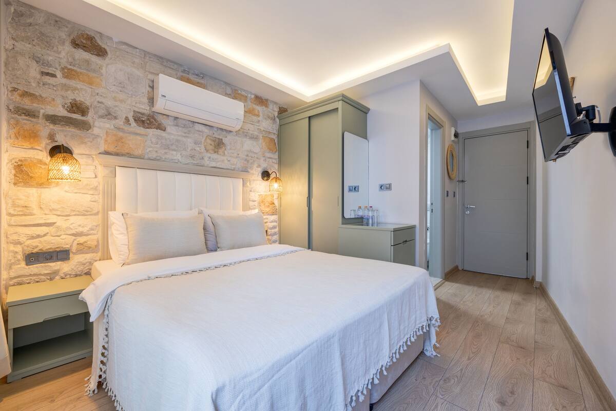 Ein Schlafzimmer mit Steinwand, einem Bett mit weißer Bettwäsche, einem Nachttisch, einem Spiegel und einem angebrachten Fernseher.