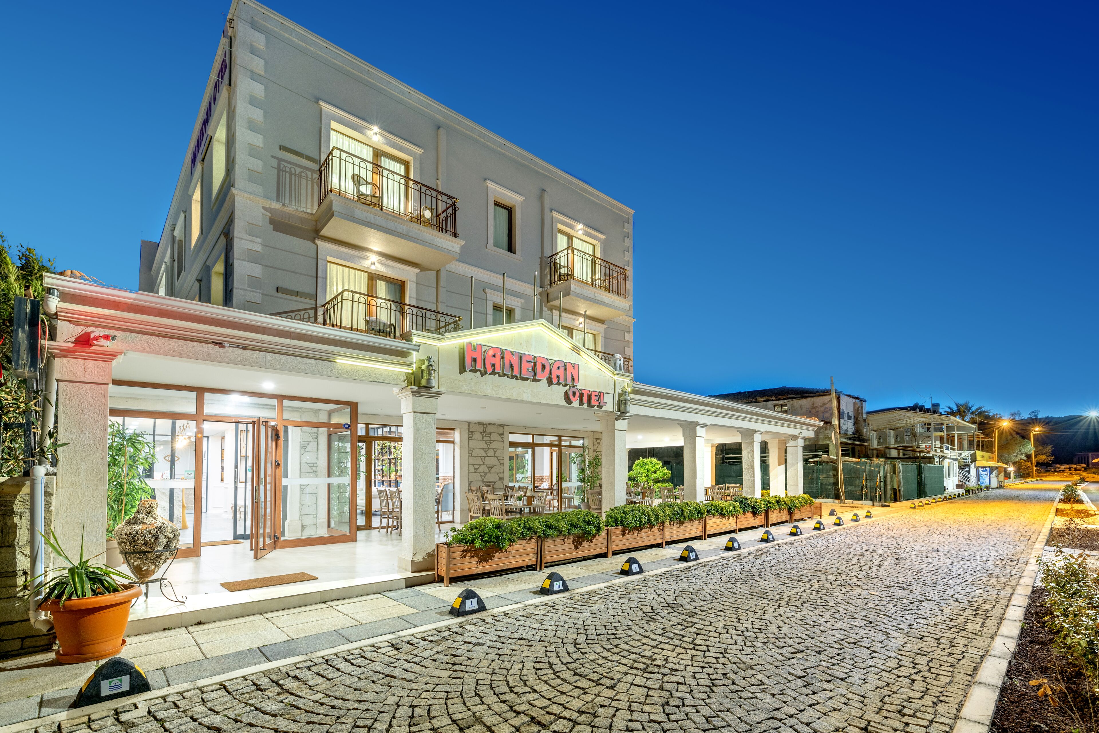 A hotel with a modern facade, a well-lit entrance, and a cobblestone street in front.