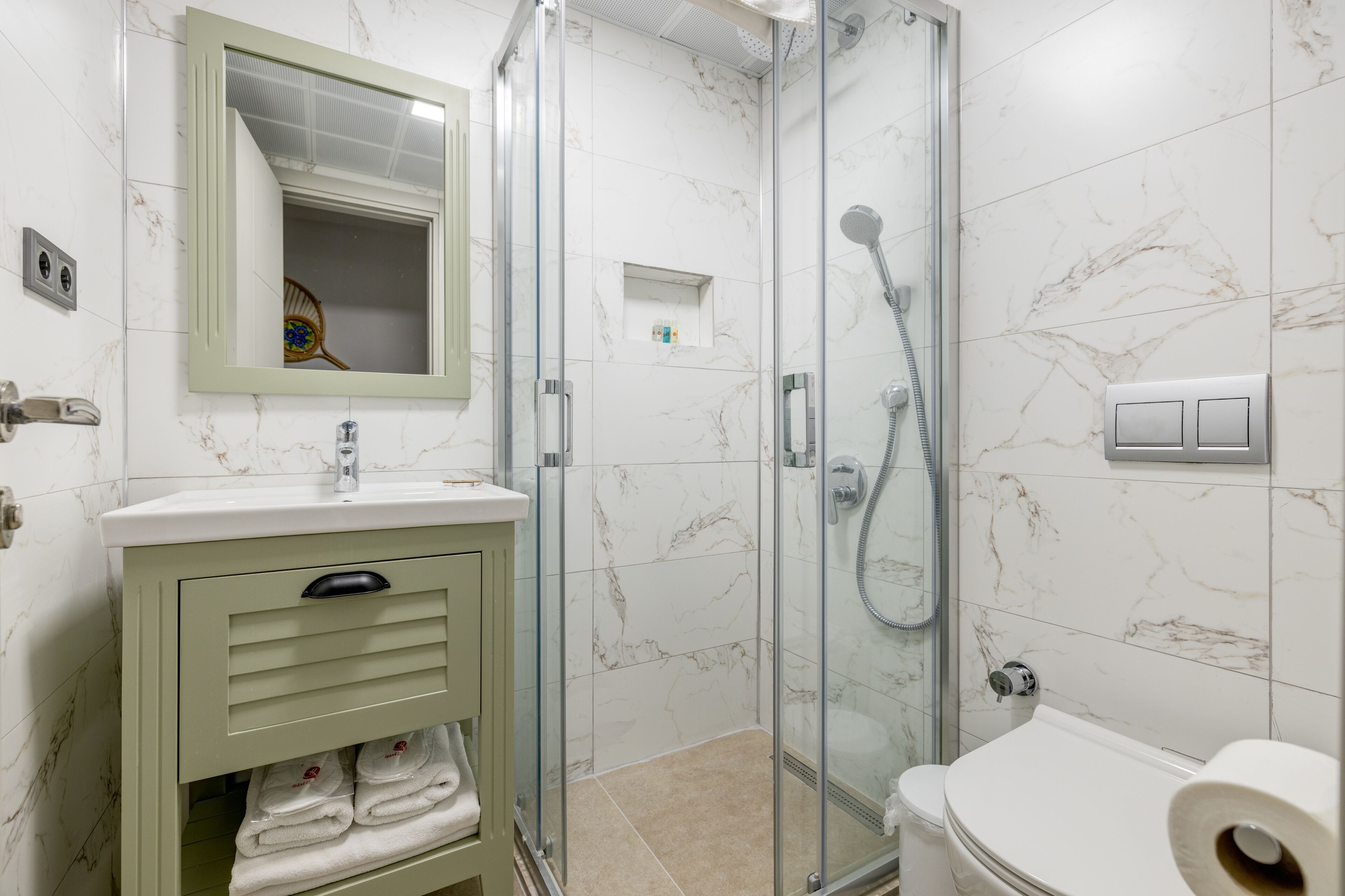 A bathroom with a glass-enclosed shower, a toilet, a sink with a mirror, and a cabinet with towels.