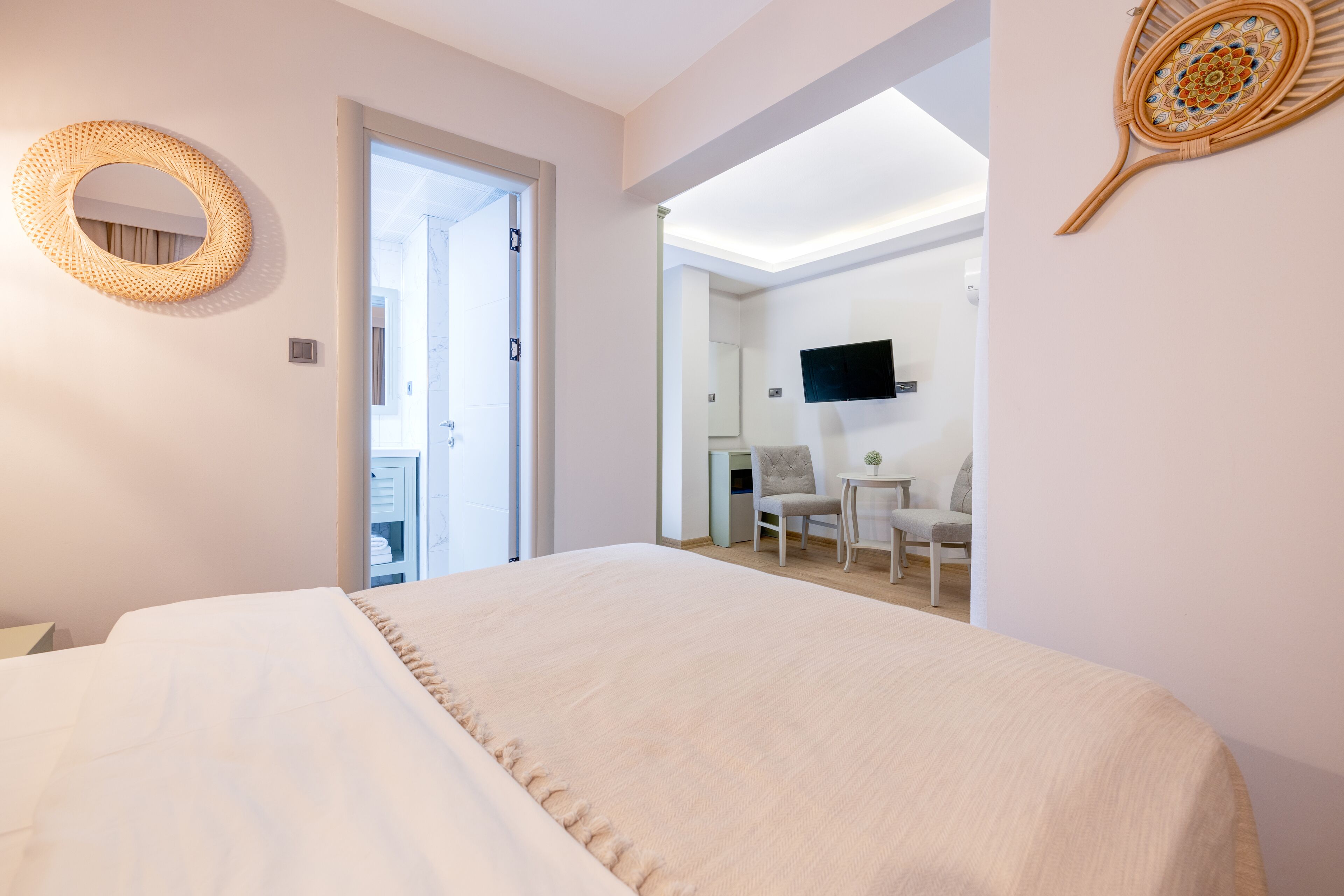 A bedroom with a large bed, a round mirror, a television mounted on the wall, and a door leading to a bathroom.