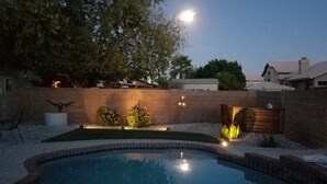 Um quintal com piscina, muro de tijolos e uma árvore.