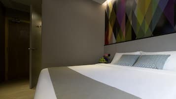 Ett modernt hotellrum med en stor säng, ett geometriskt konstverk på väggen och ett litet sidobord med en vas med blommor.