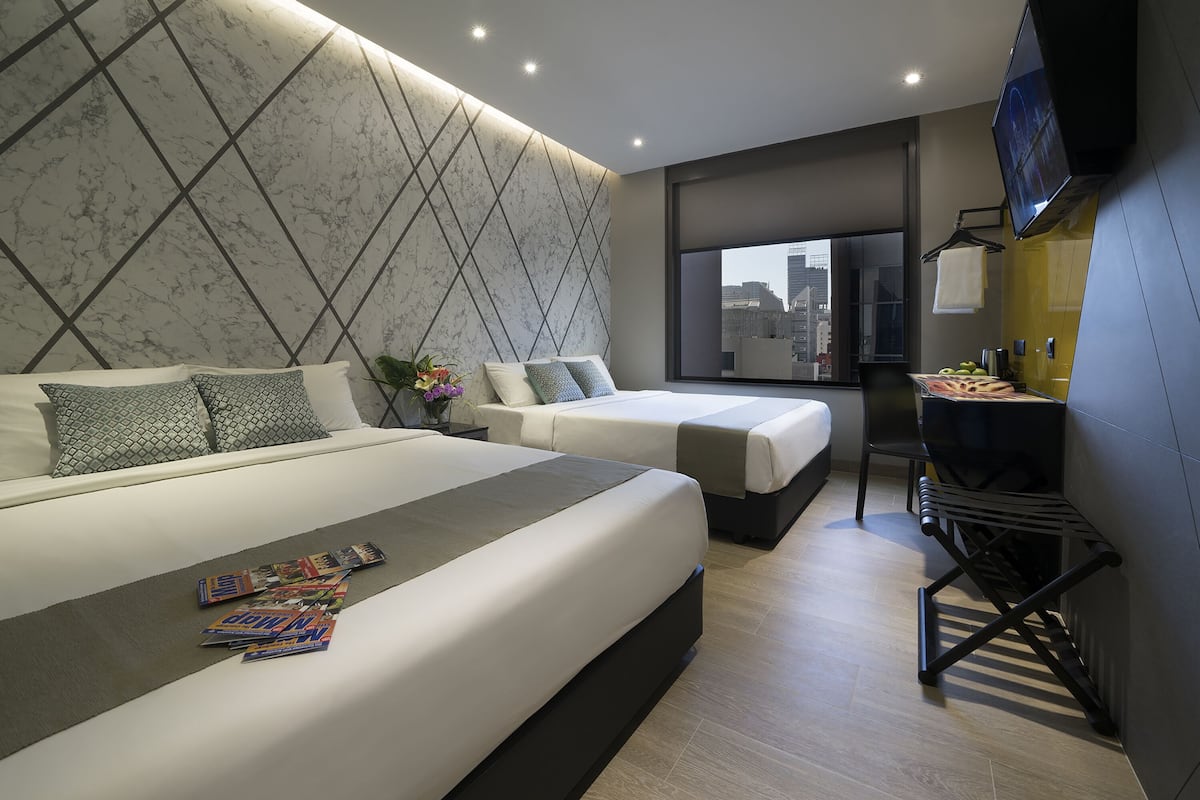 A modern hotel room with a large bed, two smaller beds, a desk, and a TV.