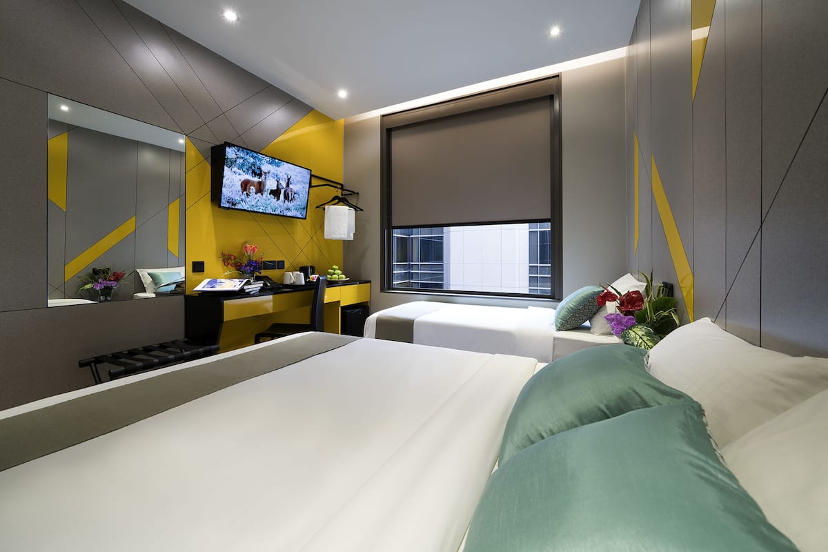 A modern hotel room with a large bed, a desk with a computer, a television, and a window with a view of the city.