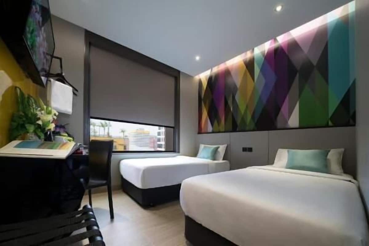 A modern hotel room with a desk, two beds, a large window, and a colorful geometric wall art.