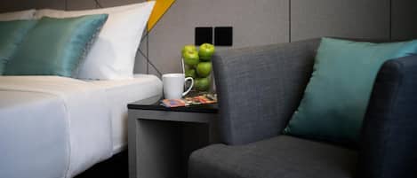Una habitación de hotel moderna con una cama, una mesita con una revista, una taza y un bol de manzanas.