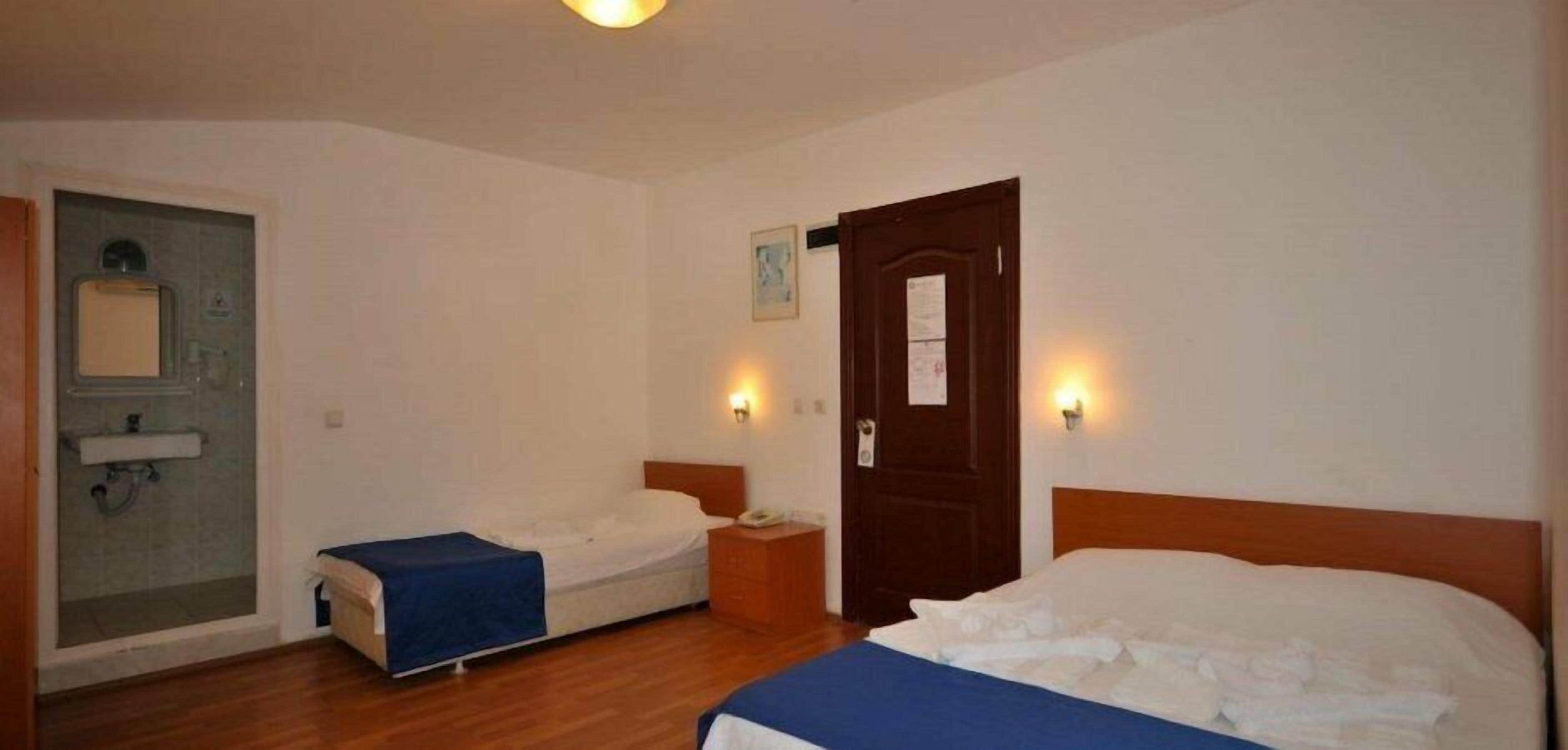 A hotel room with two single beds, a small table, a nightstand, a door, and a shower area.
