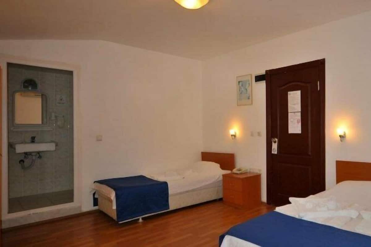 A hotel room with two single beds, a small table, a nightstand, a door, and a shower area.