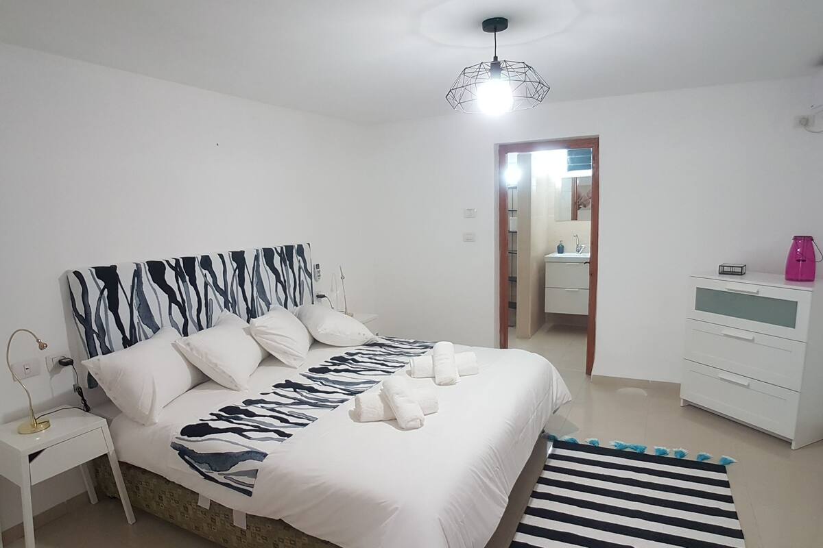 A bedroom with a bed, bedside table, dresser, and a bathroom visible through an open door.