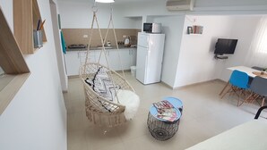 A modern kitchen with a hanging chair, a dining area with a table and chairs, and a refrigerator. - Hili Apartments (Tiberias)