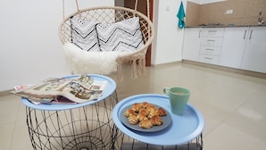 A kitchen with a hanging chair, a table with a magazine, a plate of pastries, and a mug. - Hili Apartments (Tiberias)