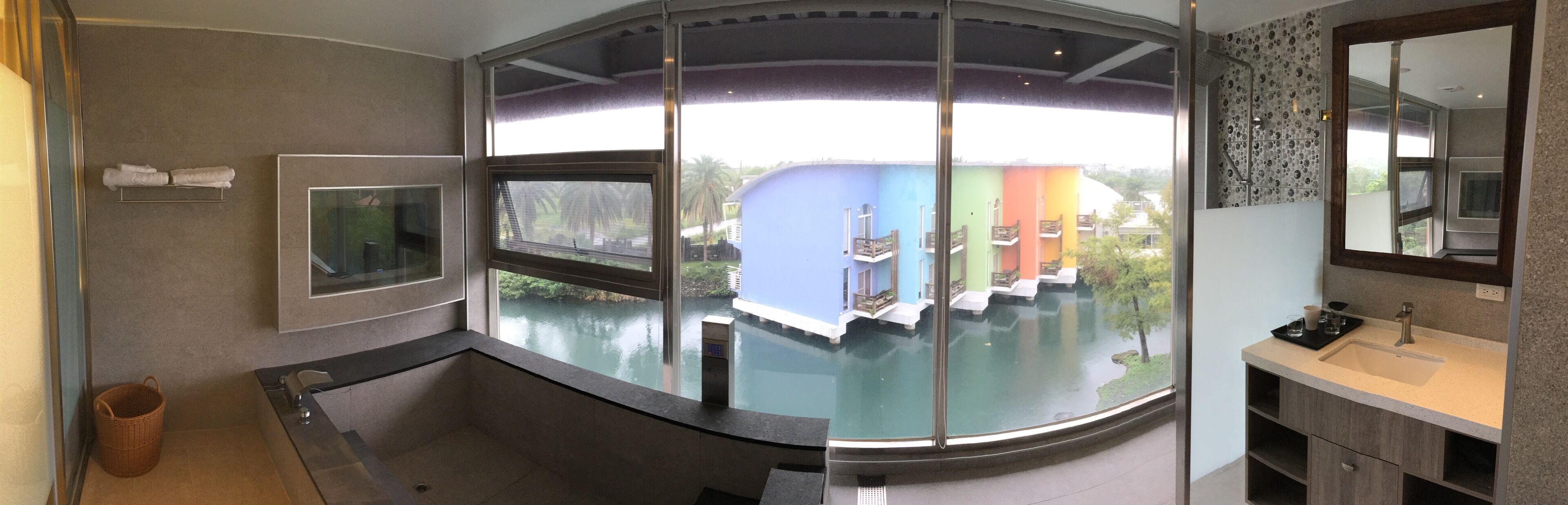 Une salle de bain moderne avec une douche à parois de verre, une grande fenêtre et une vue sur des bâtiments aux couleurs vives.