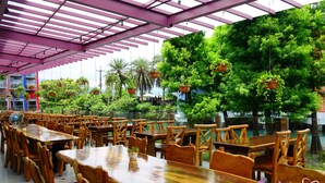A spacious outdoor dining area with wooden tables and chairs, surrounded by lush greenery and hanging planters.