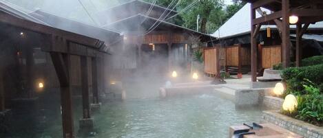 En traditionel japansk onsen med krystalklart varmt kildevand, trækonstruktioner og stenhager.