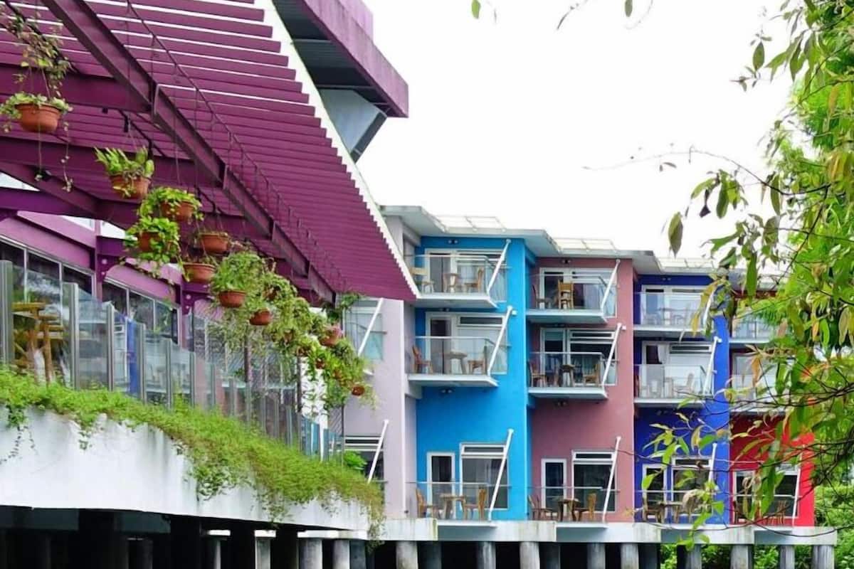 A multi-story building with balconies, a water body in front, and potted plants on the exterior.
