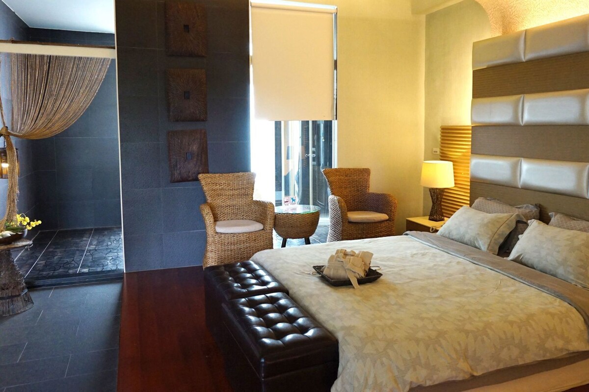 Habitación de hotel con una cama grande, un área de descanso con sillas, una mesita y un adorno en la pared.