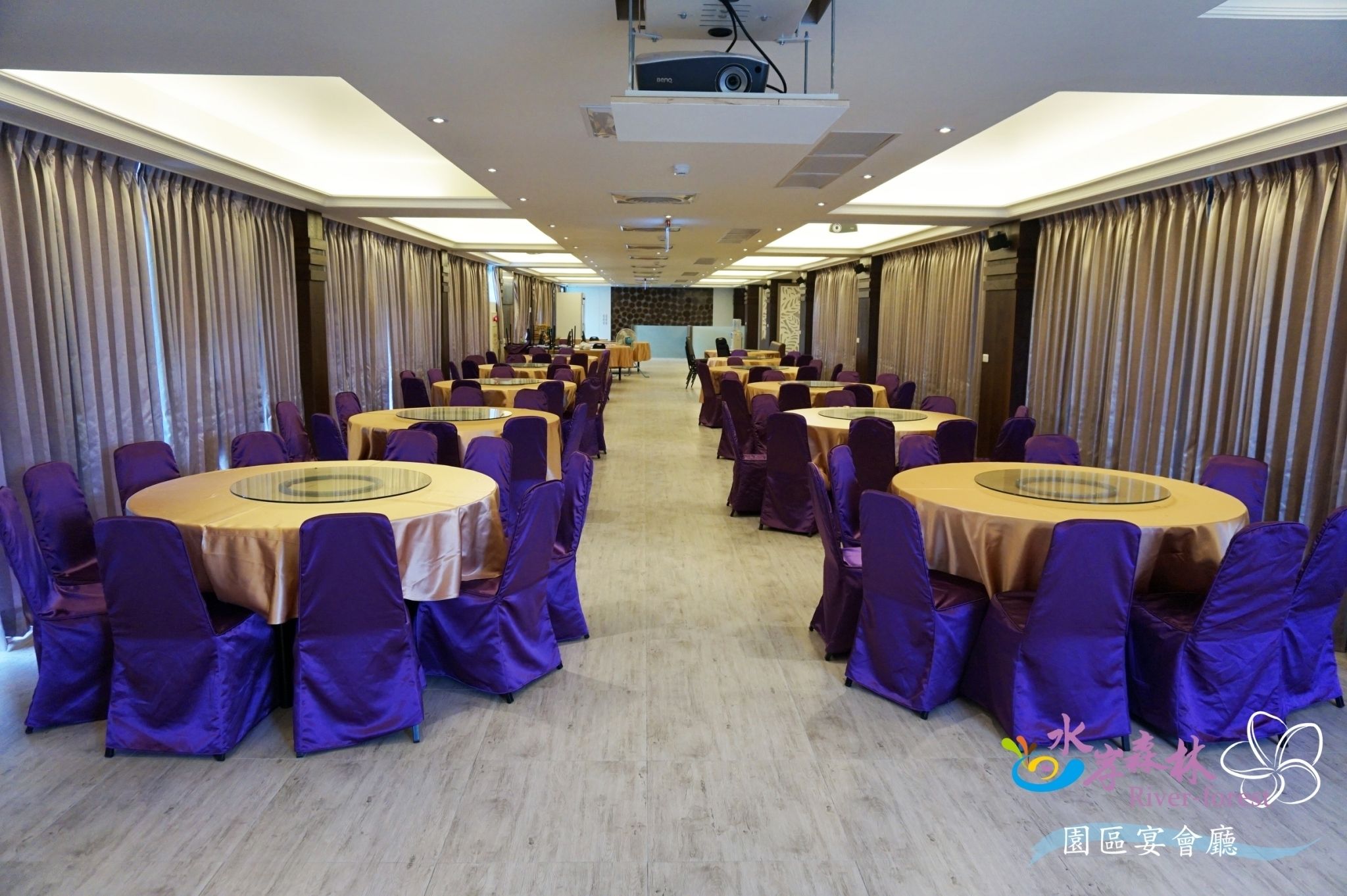 A conference room with round tables and purple chairs, equipped with a projector and a podium.