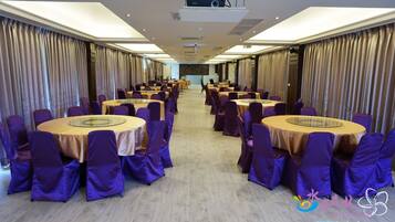 A conference room with round tables and purple chairs, equipped with a projector and a podium.