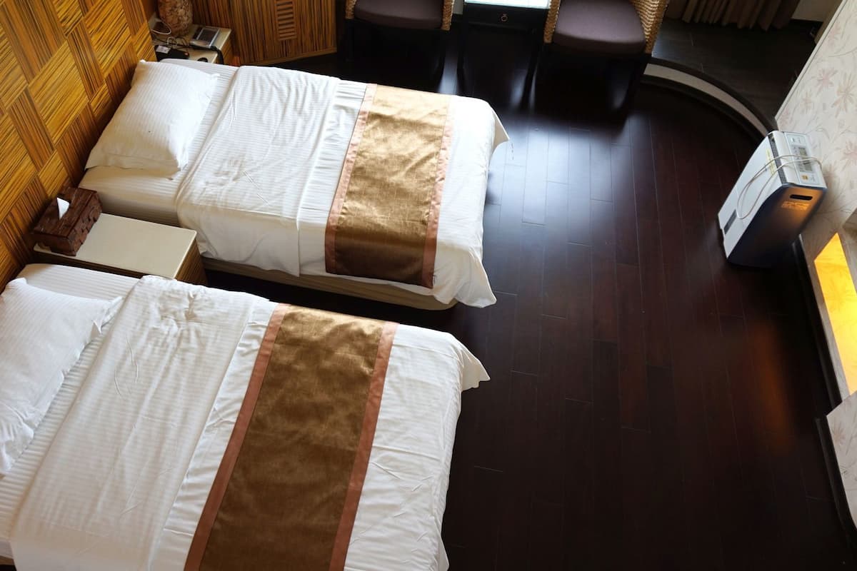 Two beds with white linens and brown decorative borders in a room with wooden paneling and a dark wooden floor.