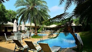 A poolside area with lounge chairs and umbrellas, surrounded by palm trees.