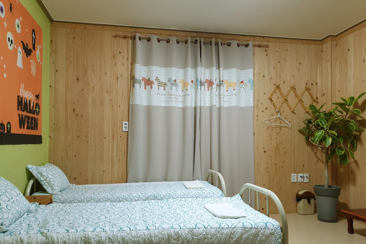 A bedroom with a bed, a chair, a potted plant, and a wooden wall.