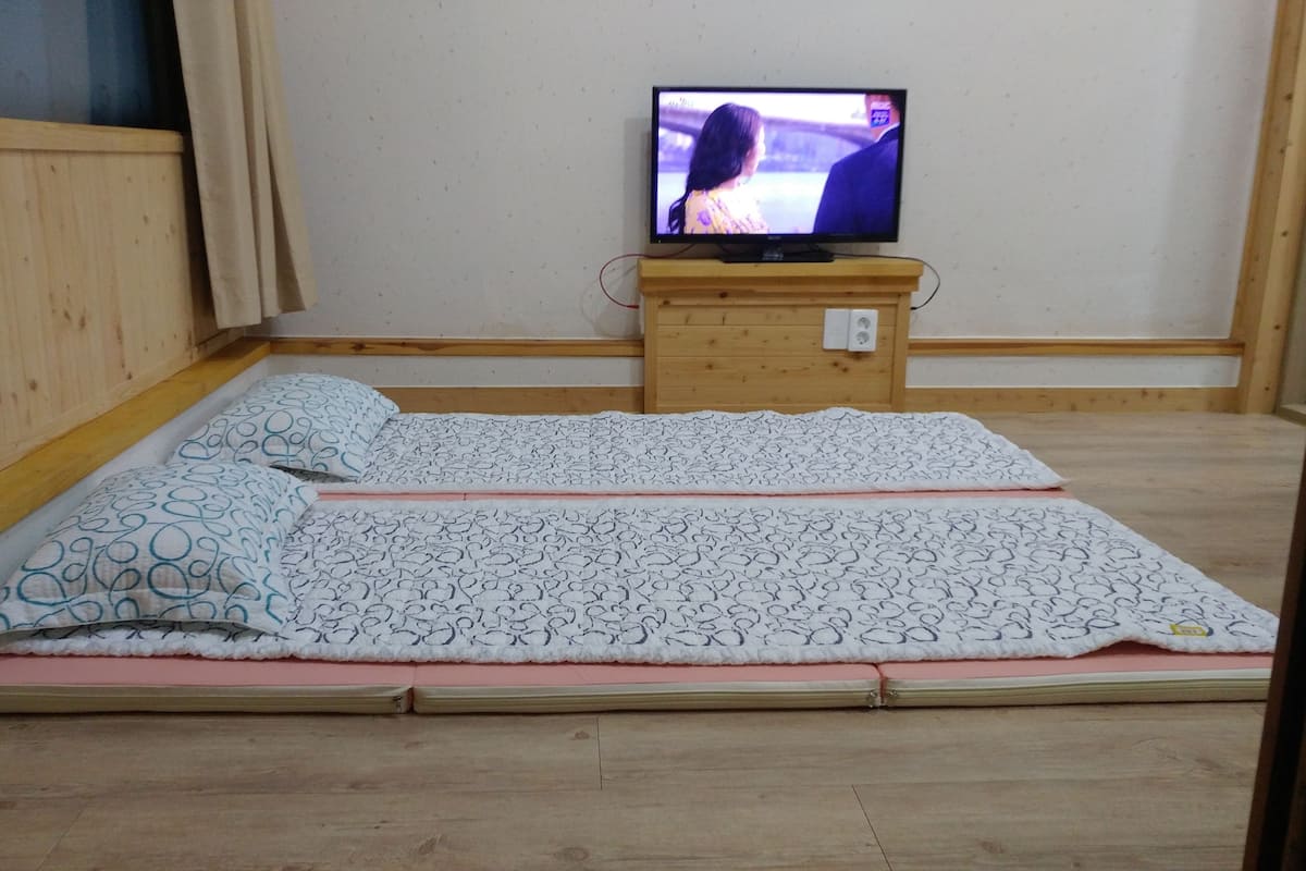 A room with a bed, a television on a wooden stand, and a wooden floor.